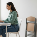 Woman working at a desk next to a folded chair in a home office.