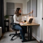 Woman in a small home office adjusts acoustic wall panels beside her desk with sound absorbing furniture in the room
